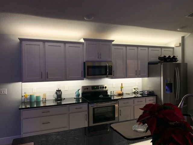 Kitchen with white cabinets, black countertops, stainless steel appliances, and under-cabinet lighting.