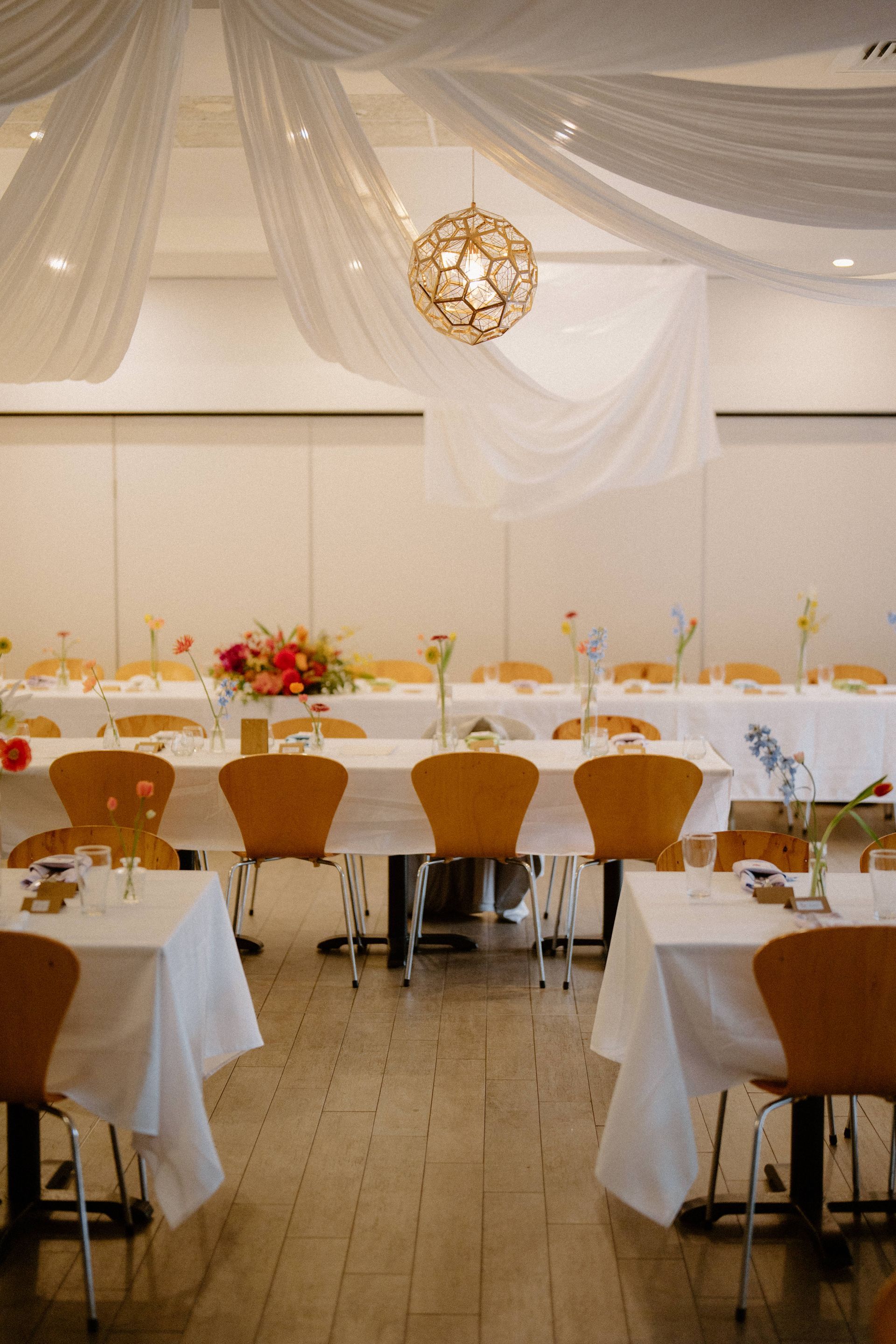 Elegant banquet hall with white drapes, gold pendant light, and set tables with brown chairs — Top Point Café In East Gosford, NSW