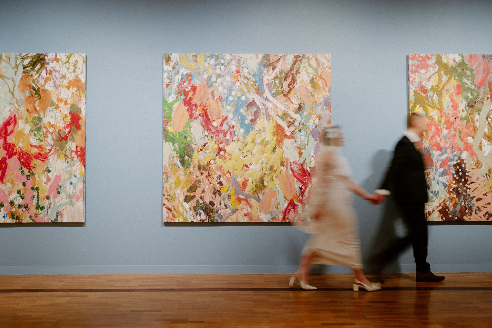 Two blurred people walking past colorful abstract paintings in a gallery — Top Point Café In East Gosford, NSW