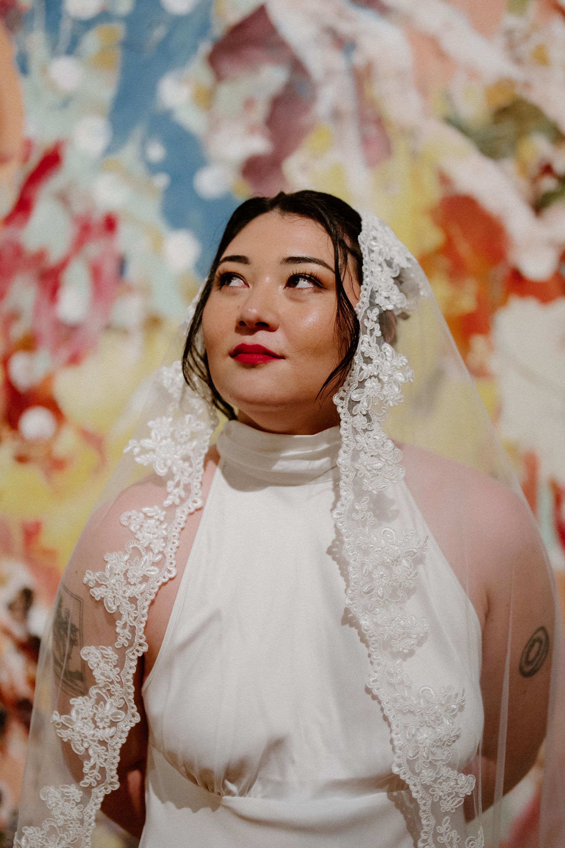 Woman in white lace veil and dress, gazing upward against a colorful floral mural — Top Point Café In East Gosford, NSW