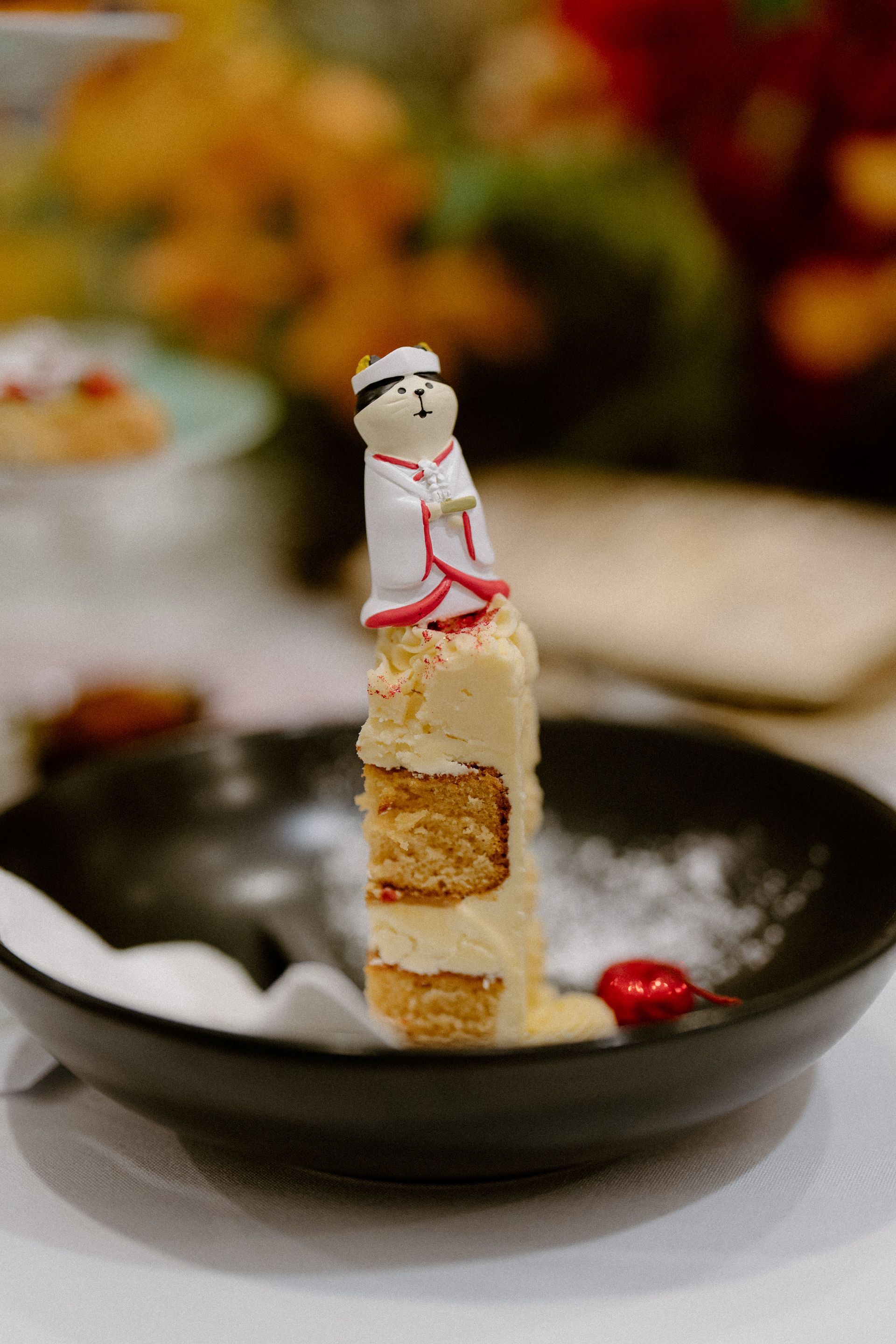 A small figurine topper sits on a layered dessert in a black dish, with a blurred table setting behind — Top Point Café In East Gosford, NSW