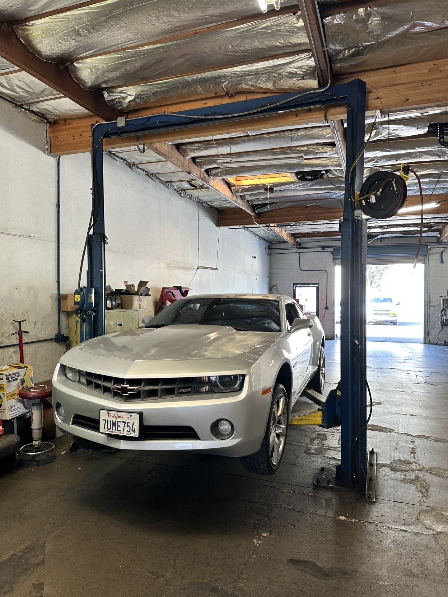 White sedan in an auto repair bay under a car lift, with garage equipment and an open doorway in back. | Agape Auto Repair