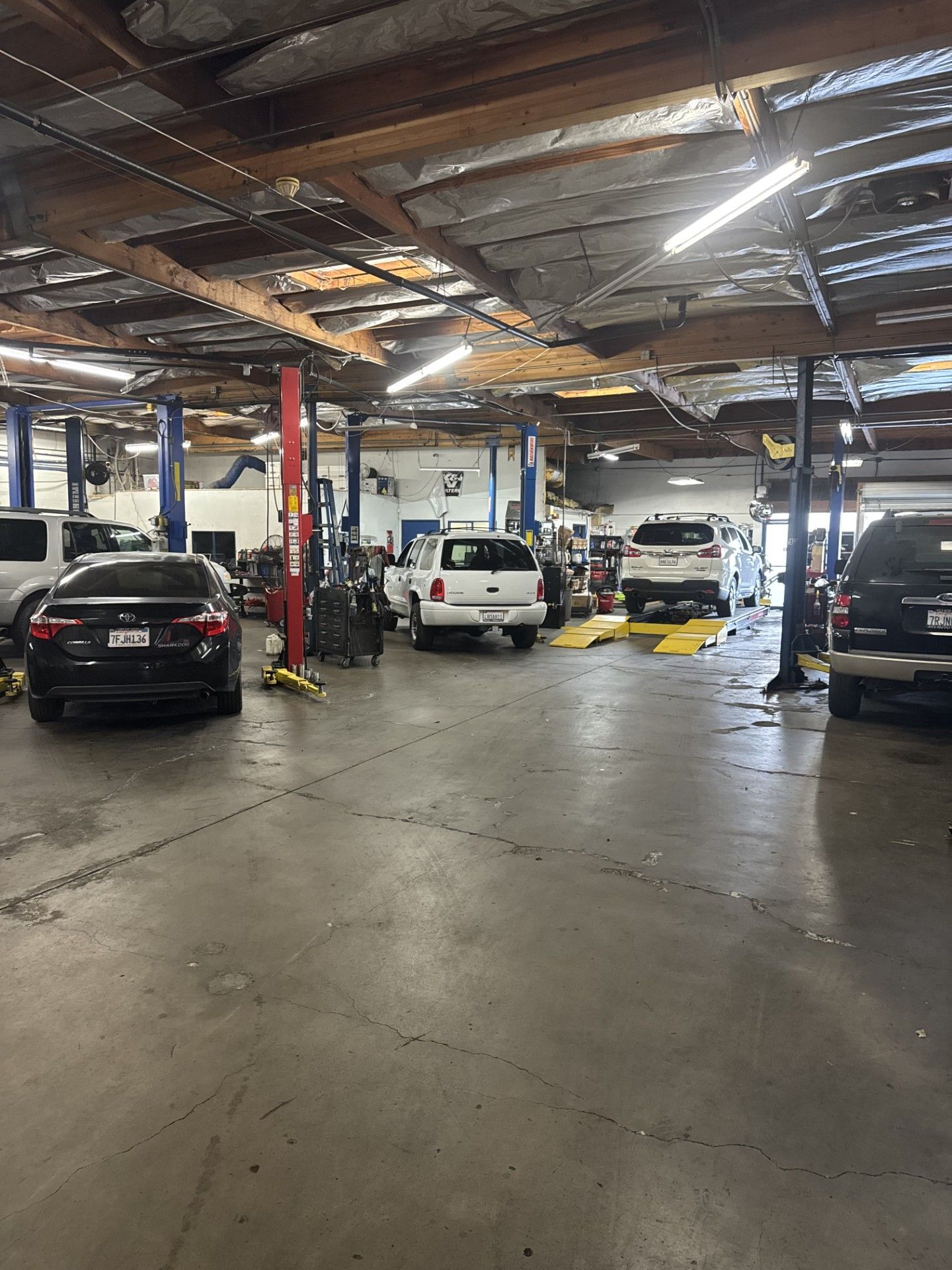 Auto repair garage with several cars on lifts and an open, industrial ceiling | Agape Auto Repair