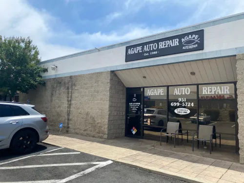 Two people in a car repair shop with lifts, cars, and a red tool cart | Agape Auto Repair
