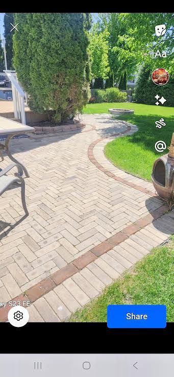 Sunny garden path with curved brick paving, grass, and tall hedges beside outdoor seating