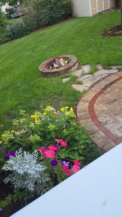 Backyard garden with lawn, flower bed, fire pit, and curved stone patio path
