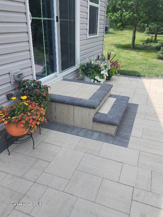 Back patio with gray pavers, steps, sliding door, and potted flowers beside a house