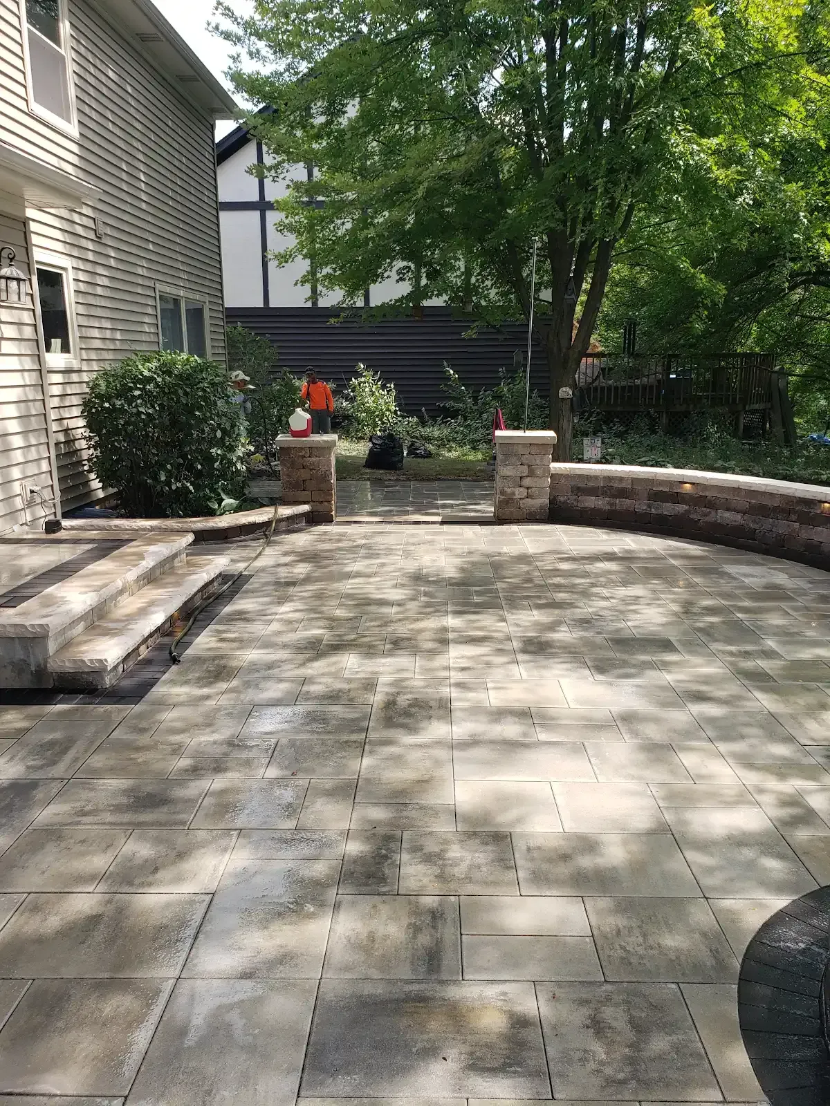 Stone patio with steps, brick planters, and a large tree beside a house