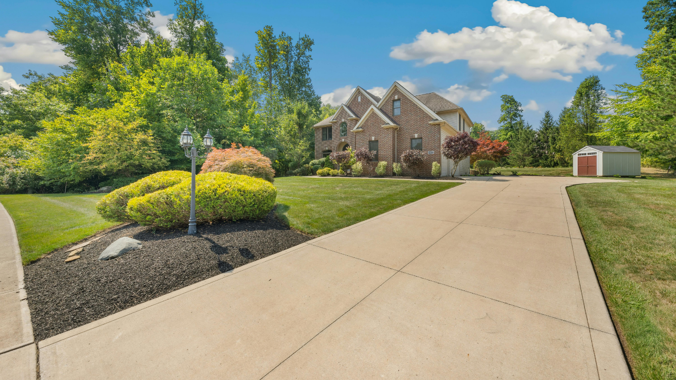 Large suburban house with a long driveway, landscaped front yard, and blue sky
