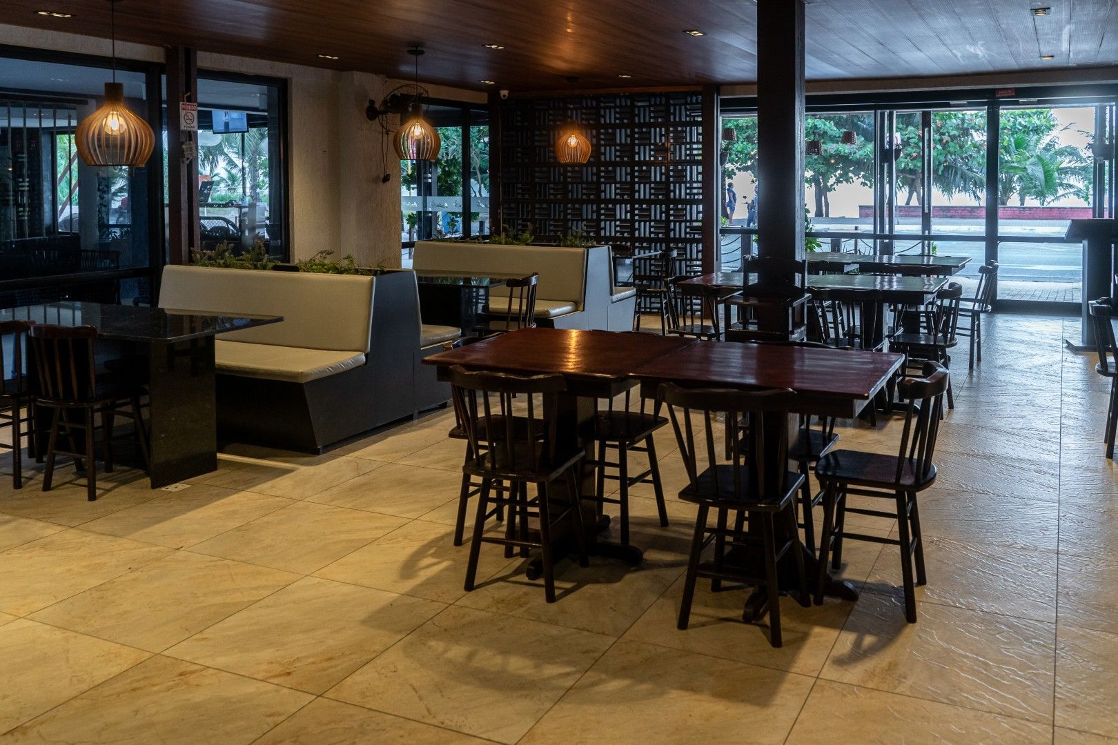 Área de jantar vazia de um restaurante com mesas, cadeiras, cabines e grandes janelas.