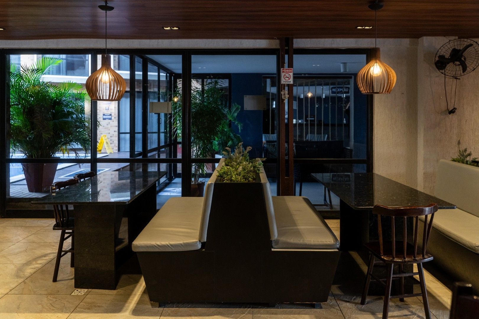 Área de jantar moderna do restaurante com uma mesa central em formato de cabine, luminárias pendentes e portas de vidro que dão para um pátio.