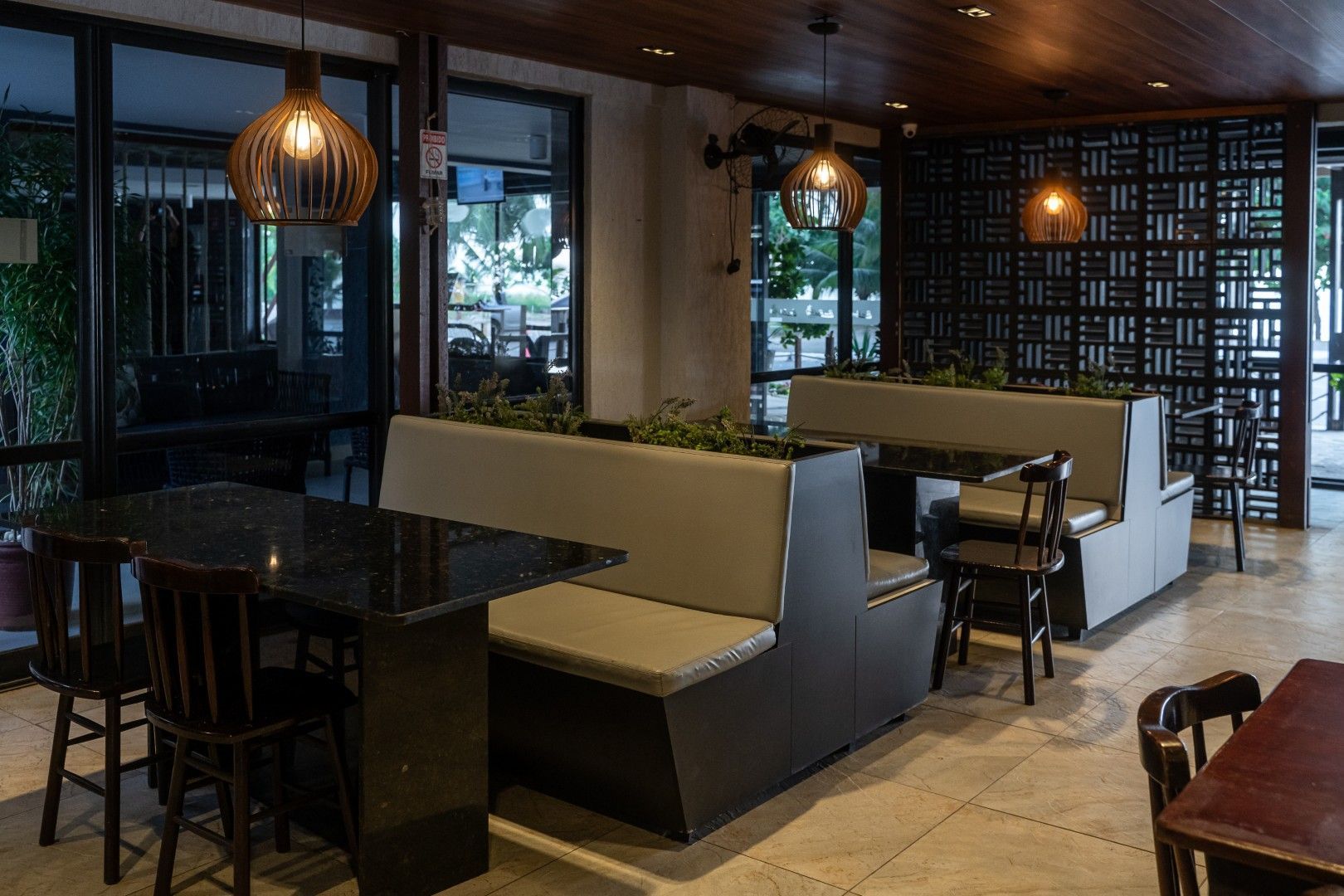 Interior de restaurante moderno com cabines, mesas pretas, luminárias pendentes e janelas amplas.