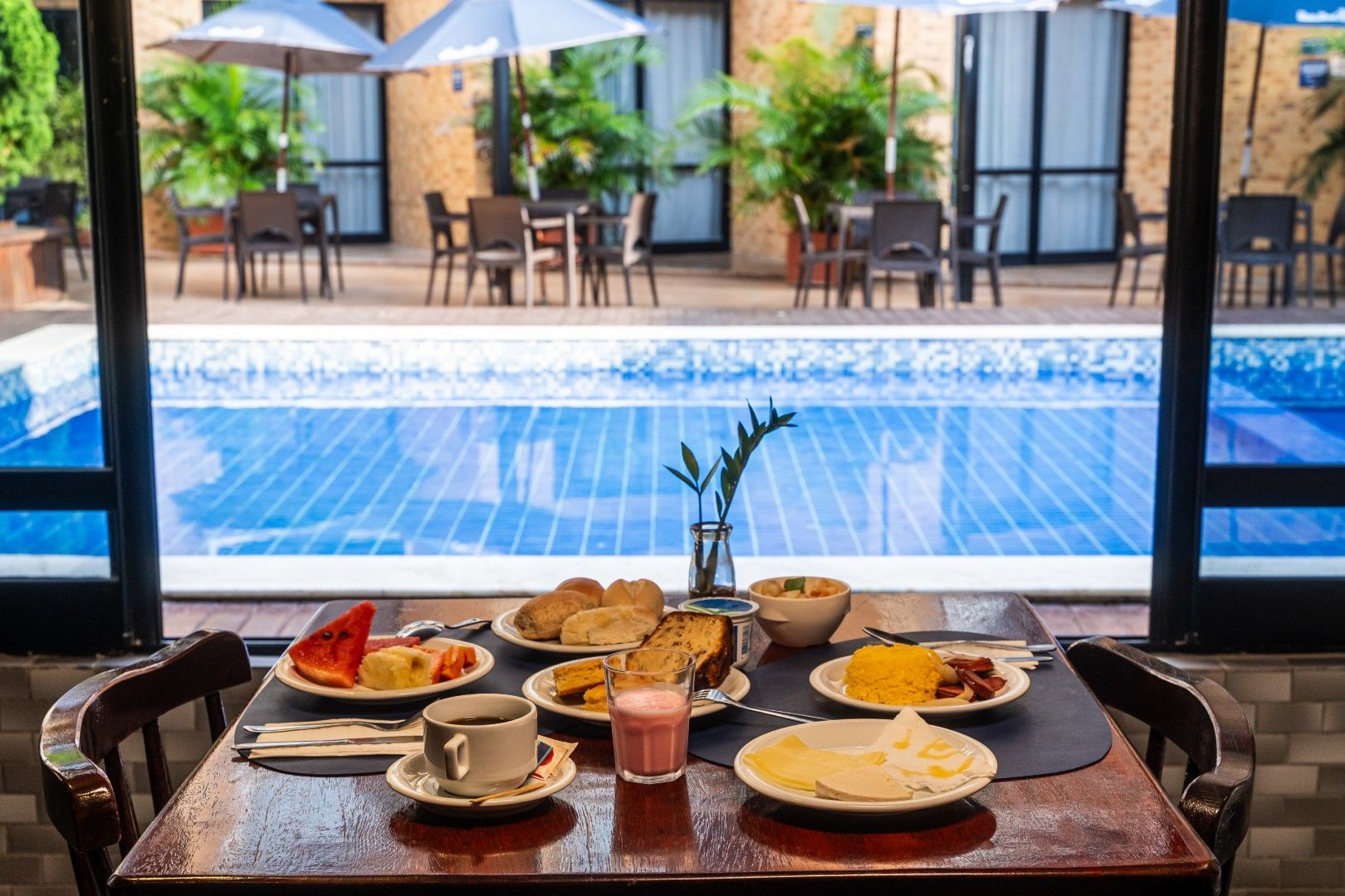 Café da manhã servido em uma mesa com vista para uma piscina azul e área de estar no pátio.