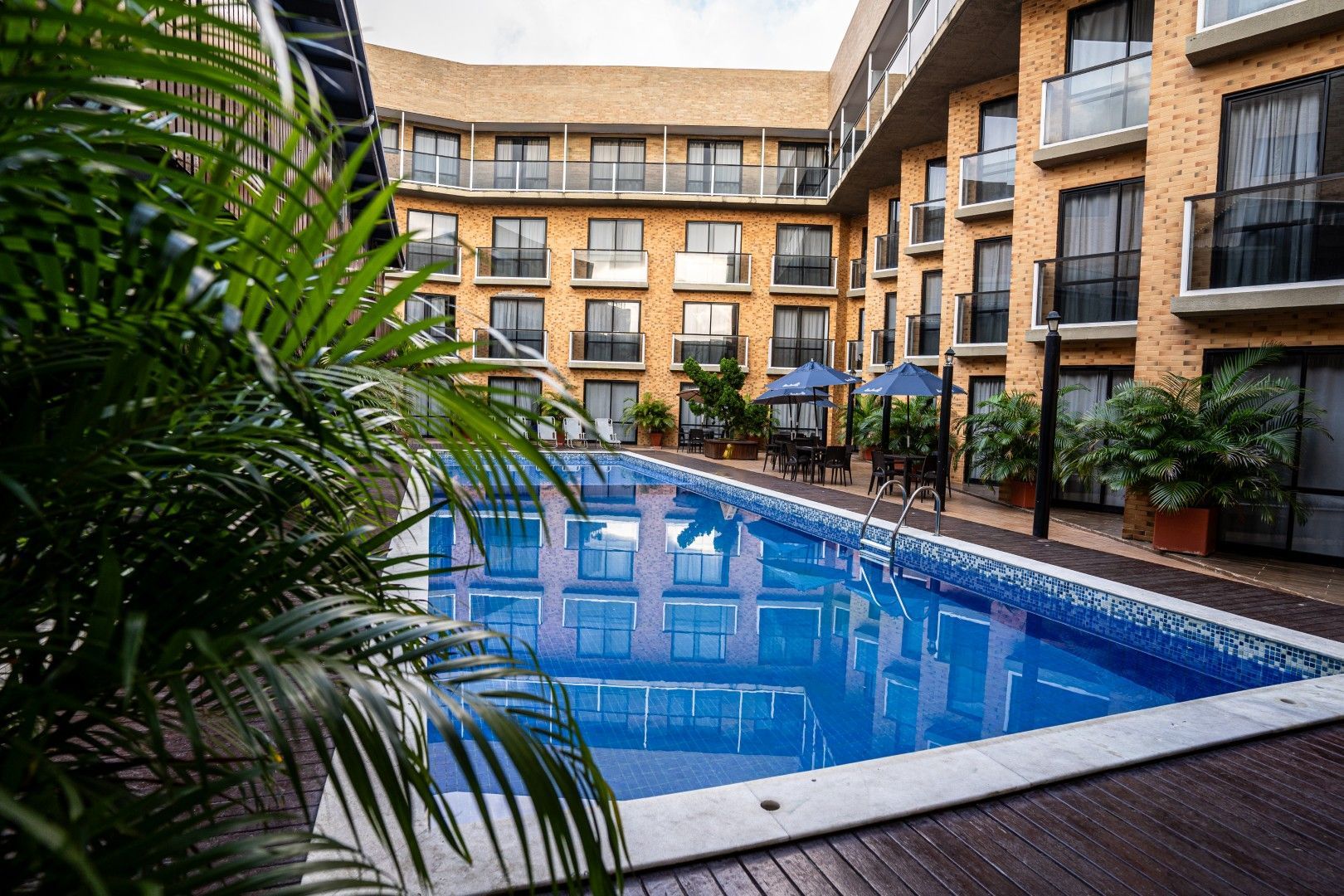 Piscina de hotel com pátio interno, água azul, palmeiras e varandas de vários andares ao redor.