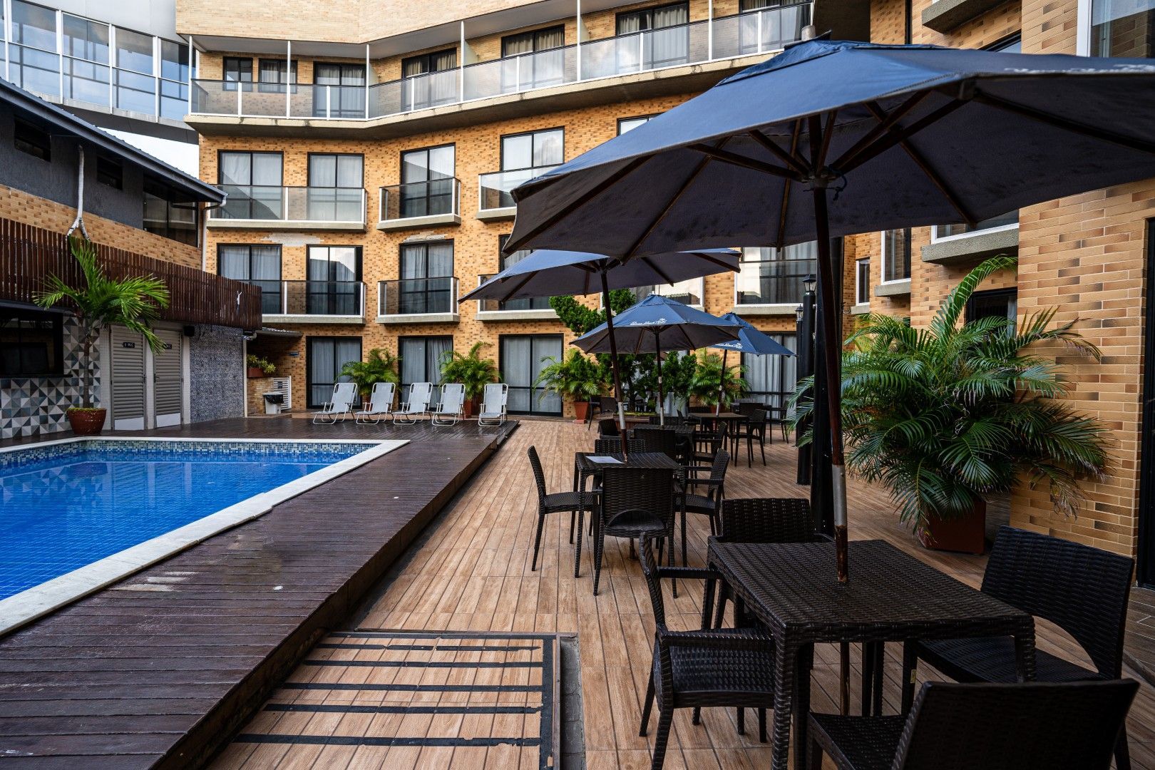 Piscina do hotel no pátio com espreguiçadeiras, guarda-sóis e deck de madeira ao lado de apartamentos modernos.