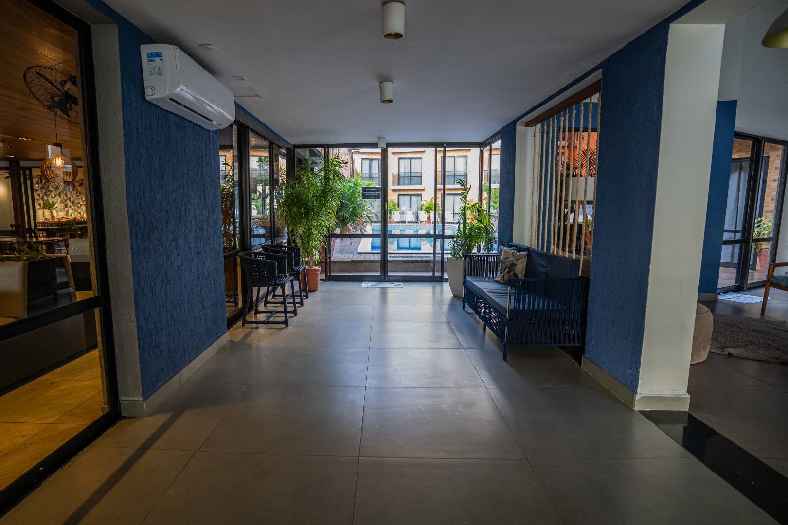 Corredor interno vazio com paredes azuis, piso de azulejo, bancos e janelas ao fundo.