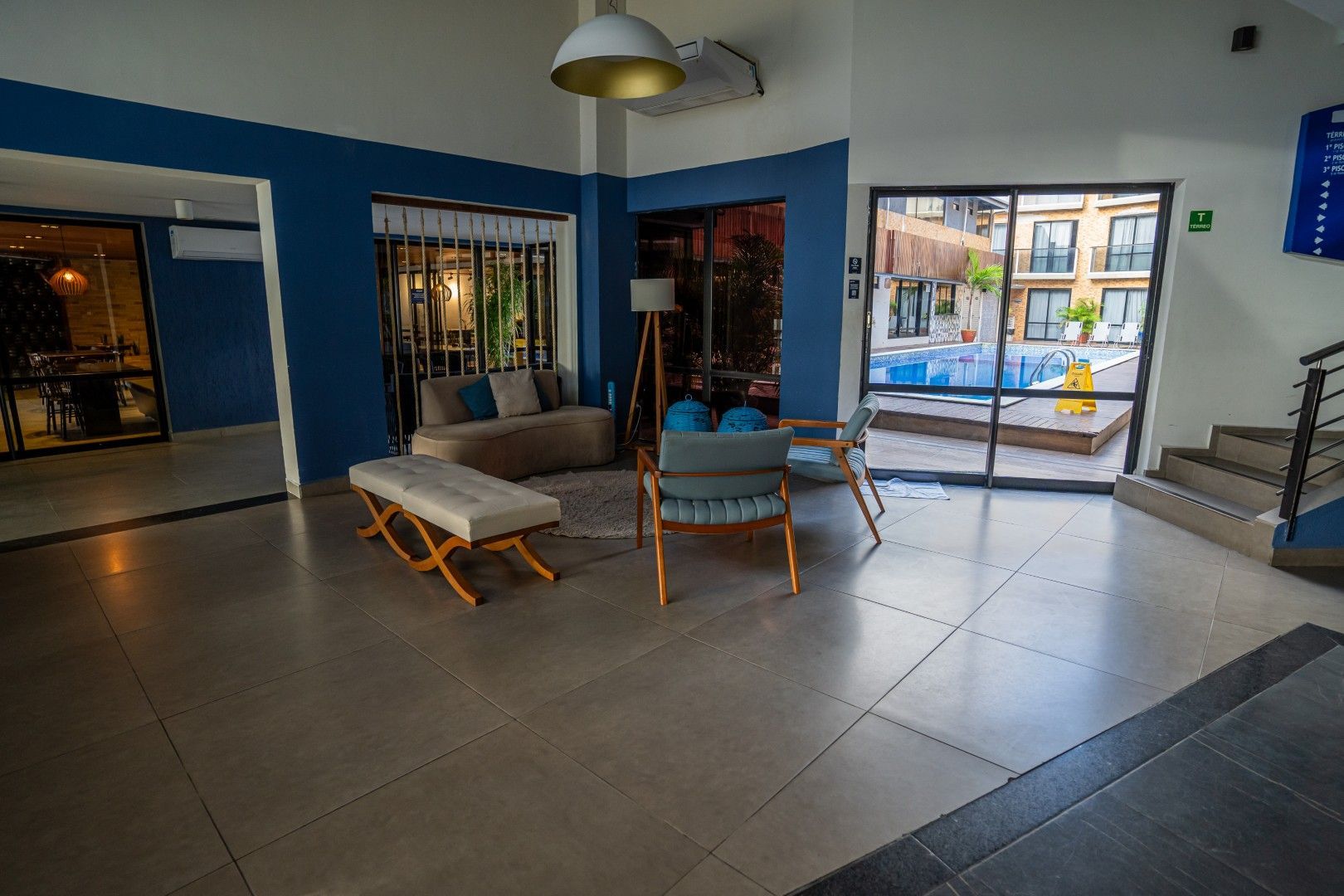 Hall de entrada moderno com paredes azuis, poltronas, janelas amplas e uma escada à direita.