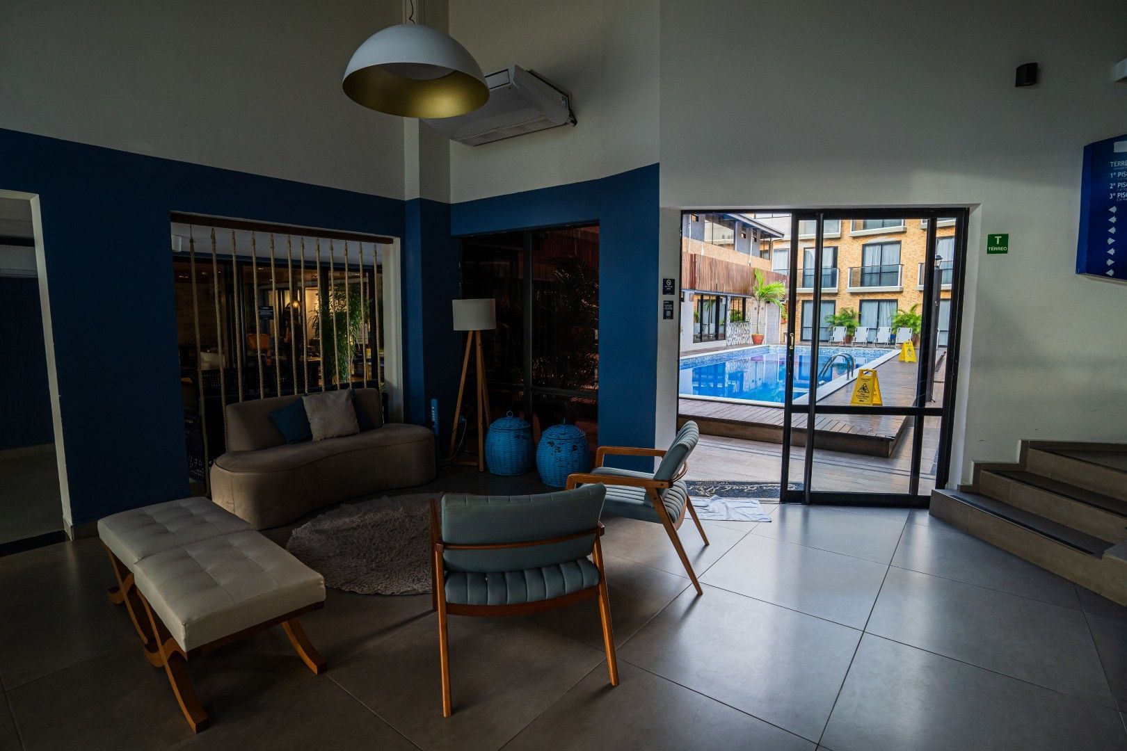 Hall de entrada moderno com sofás, cadeiras, um candeeiro, escadas e portas de vidro que dão para o exterior.