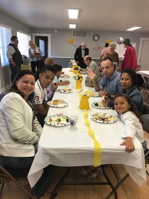 A diverse group of people sitting at a long table decorated with yellow runners and vases, enjoying a meal together.