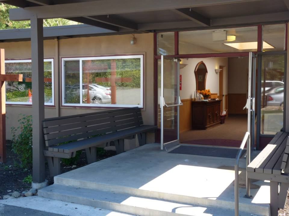 The entrance to a tan building featuring a concrete porch, two dark wooden benches, and glass double doors.