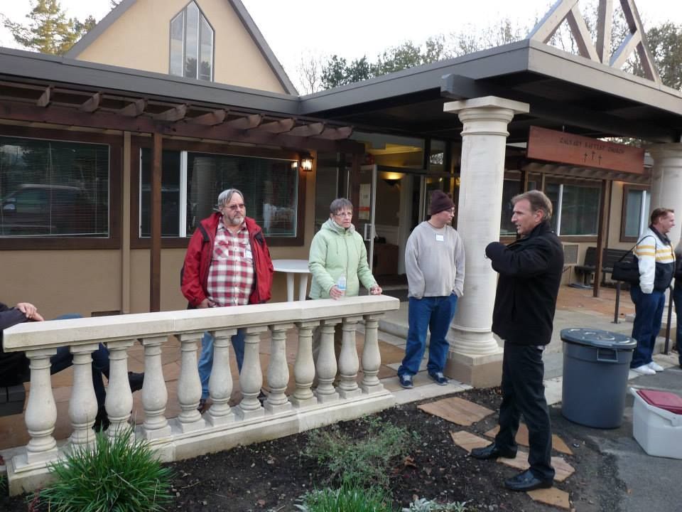 A group of people standing outside a tan building with a stone balustrade and decorative pillars.