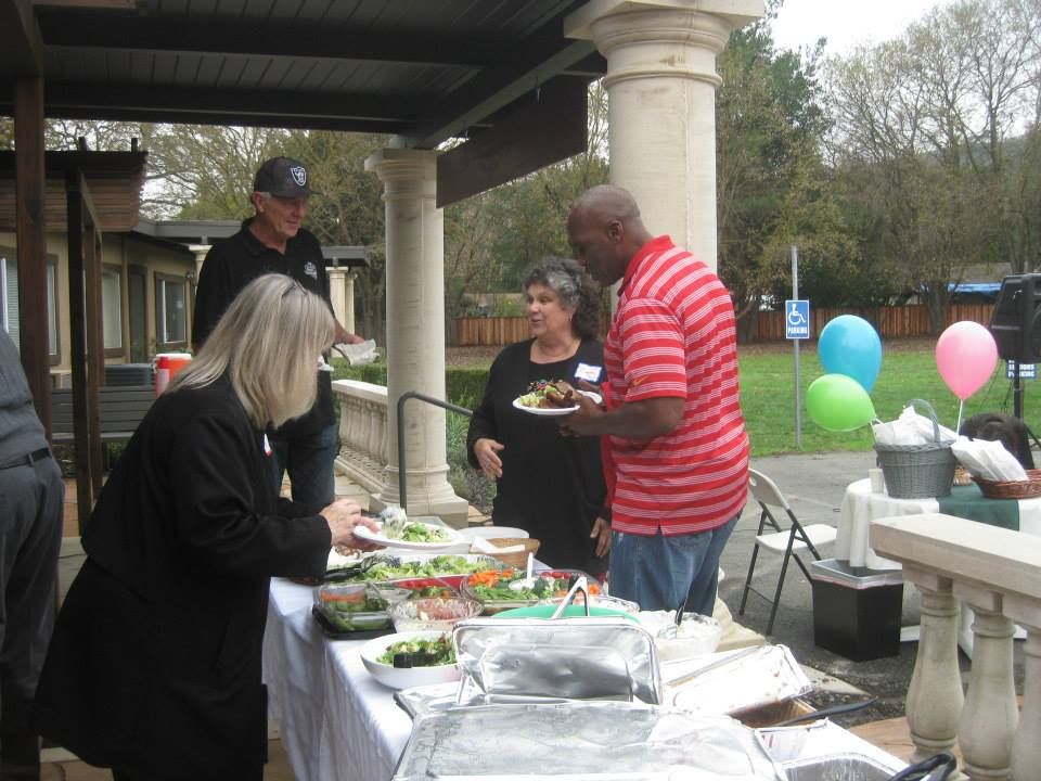 People at an outdoor buffet table with various salad dishes under a covered patio.