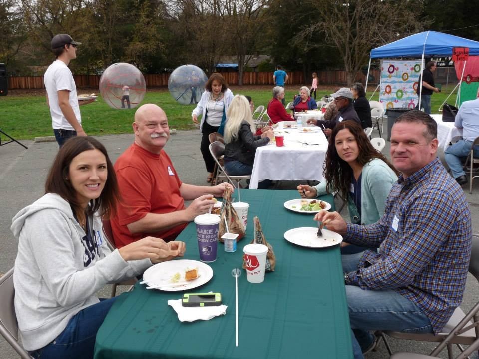 A group of people eating at tables on an outdoor patio with large transparent inflatable bubbles in the background.