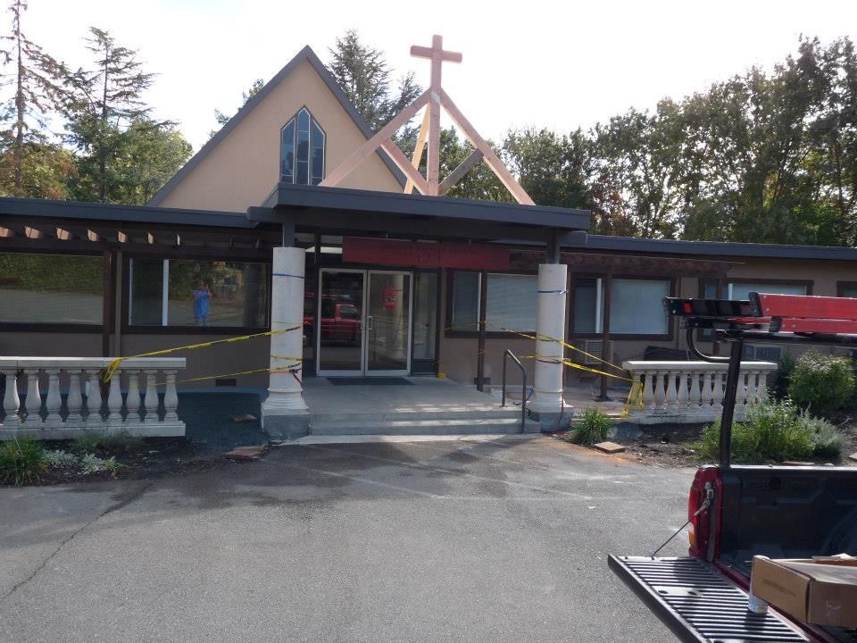 A church building entrance with a wooden cross, white pillars, and caution tape stretched across the front.