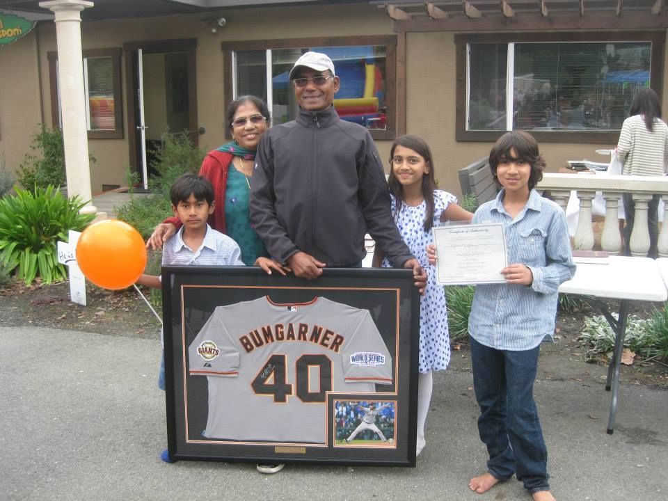 A group of five people holding a framed Madison Bumgarner jersey and a certificate outside a building.