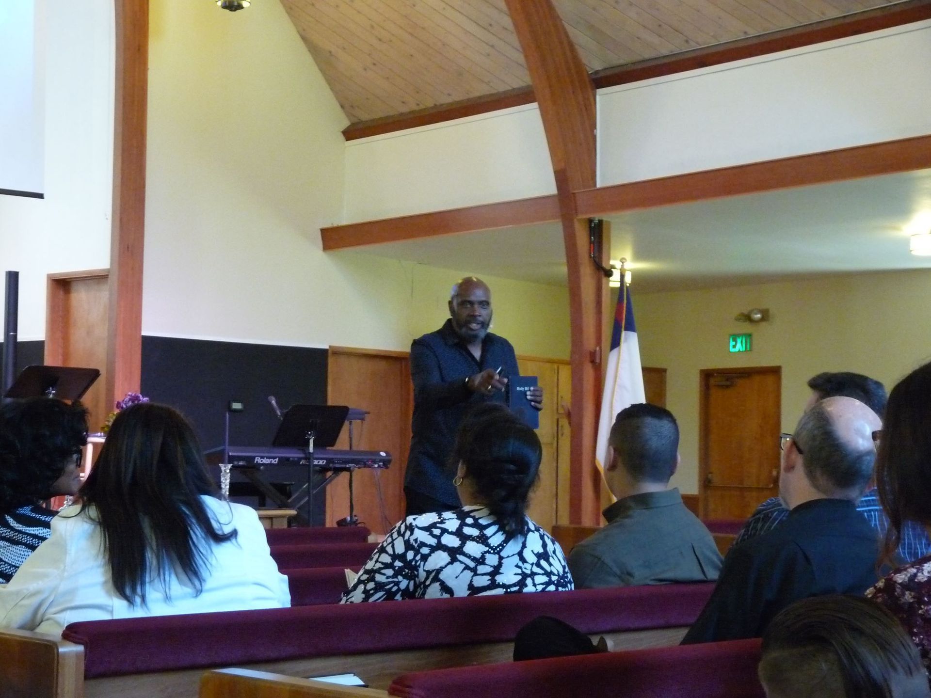 A speaker stands at the front of a church sanctuary, addressing an audience seated in wooden pews.