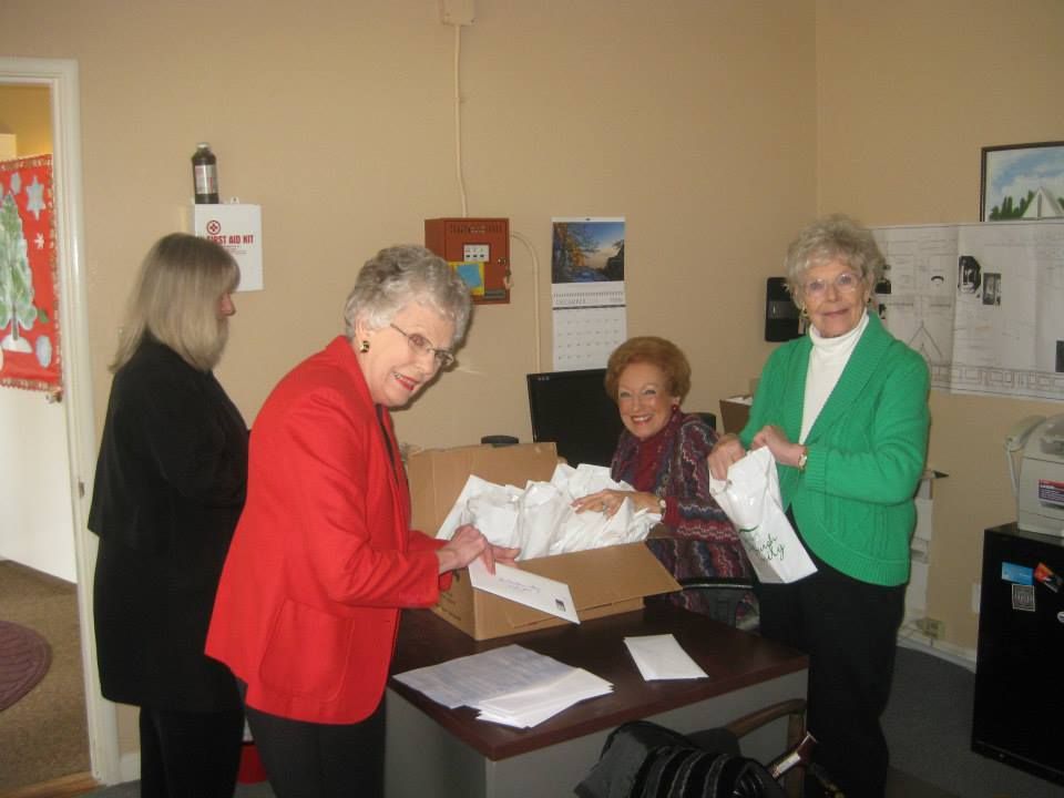 Four individuals in a bright office work together, packing white envelopes into a cardboard box on a desk.