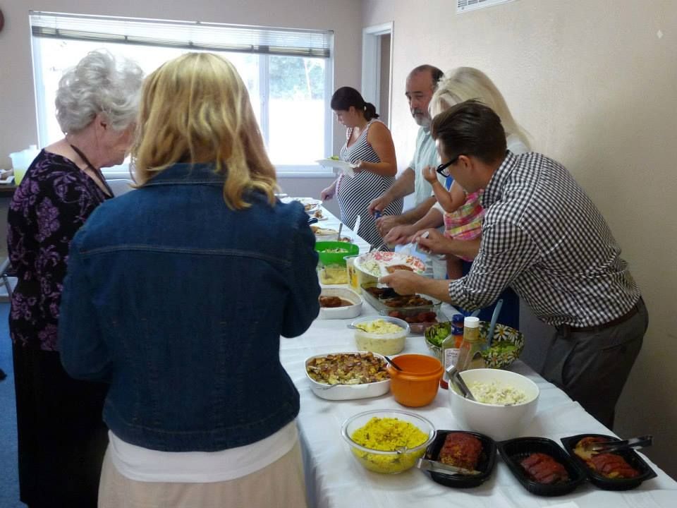 A group of people standing in a line at a buffet table, serving themselves food from various containers.