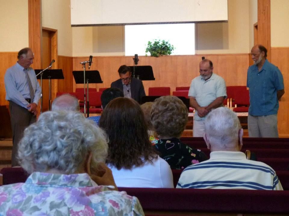 A group of people standing on a church stage, with the congregation seated in the foreground.