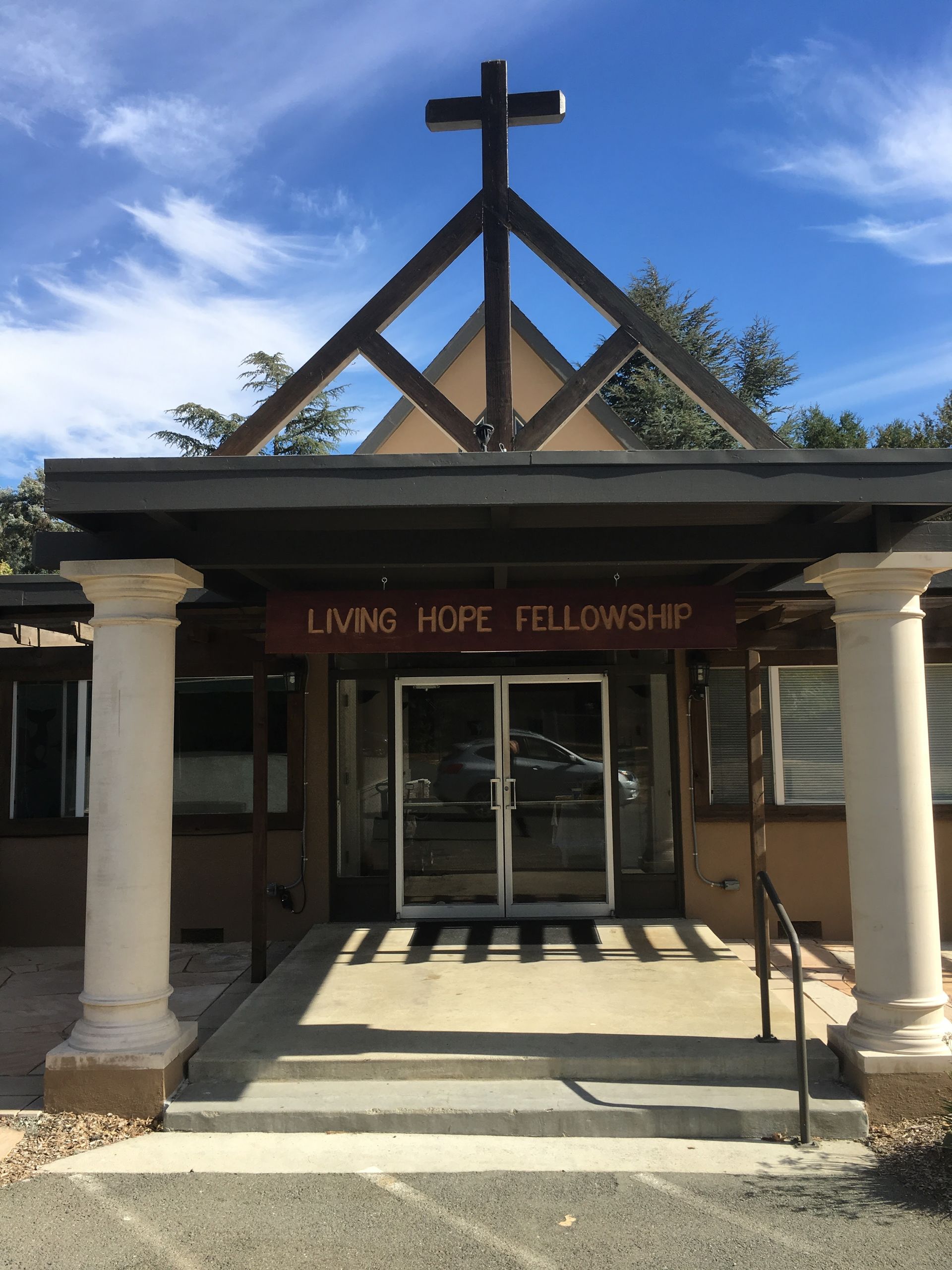 The entrance to Living Hope Fellowship, a building with a cross atop its roof, framed by two white columns.