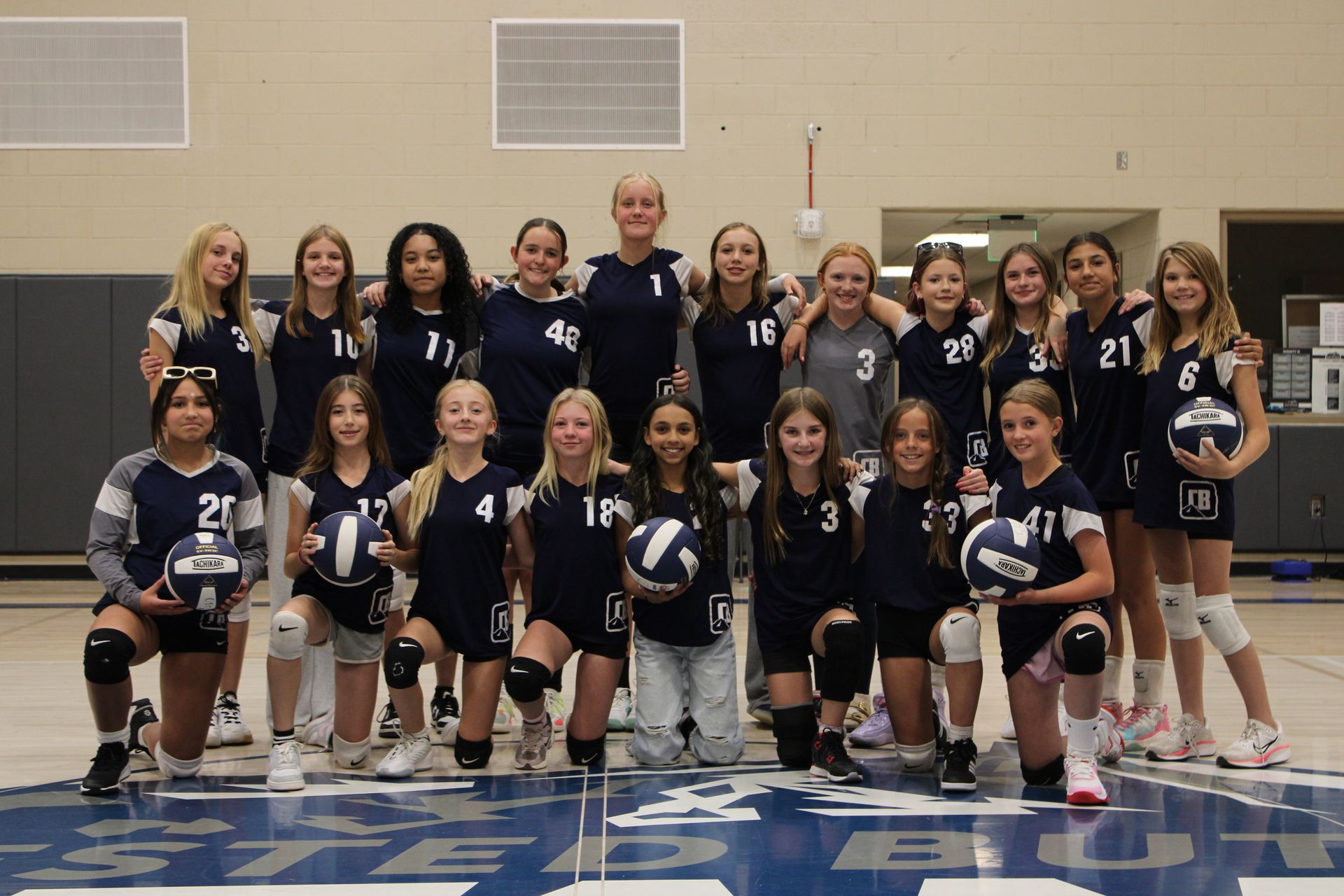 A group of young girls are posing for a picture with the word volleyball written in front of them
