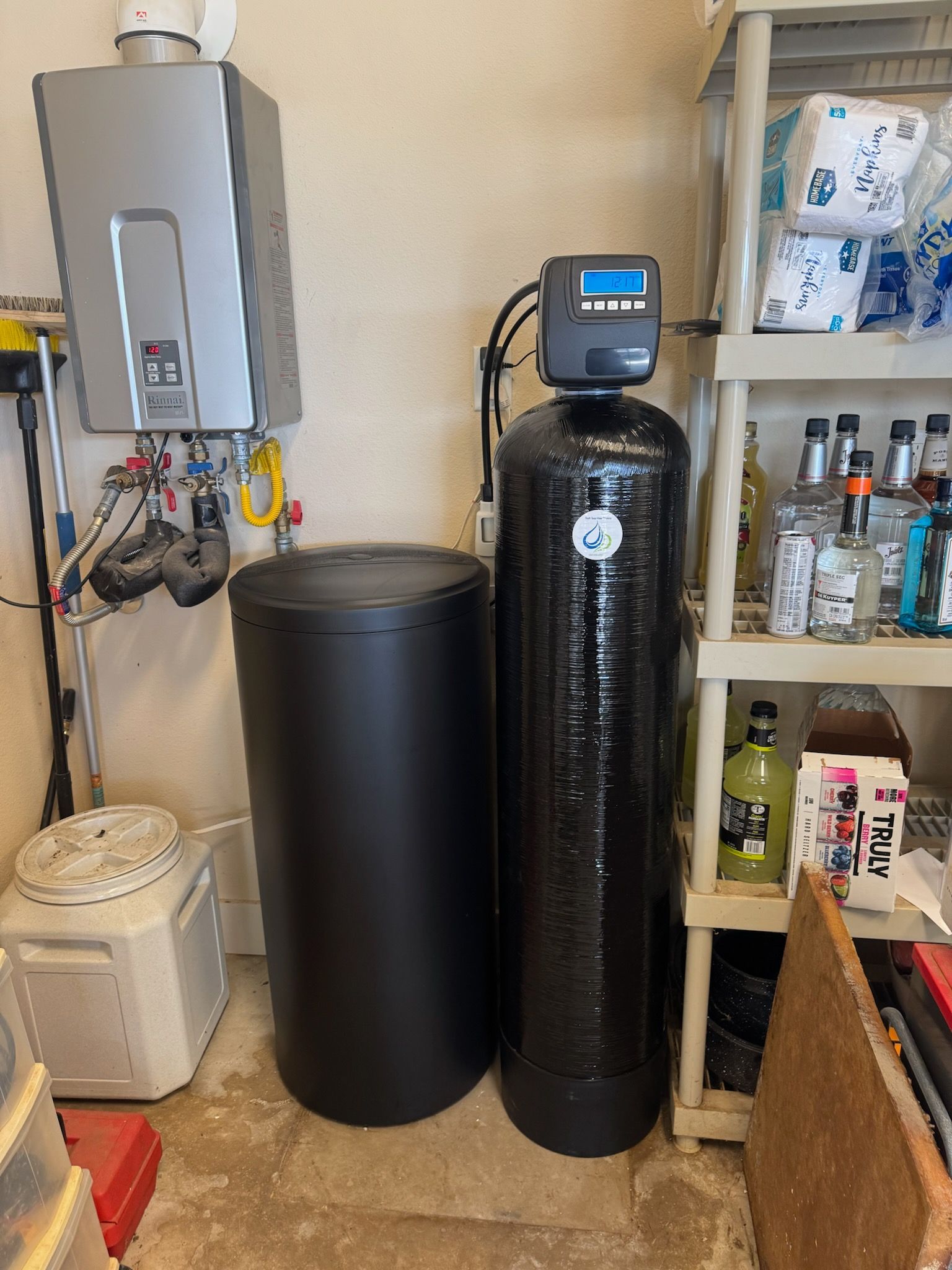 A water softener is sitting next to a water heater in a room.