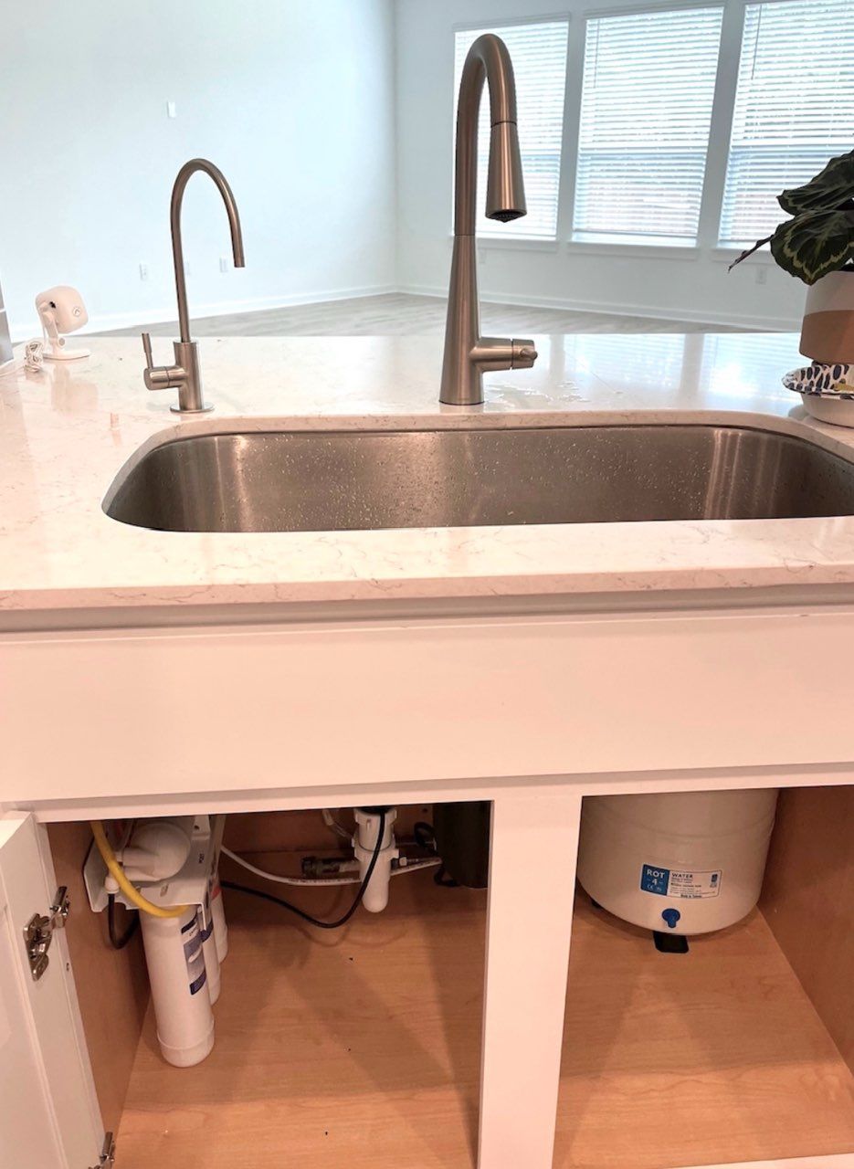 A kitchen sink with two faucets and a water filter underneath it.