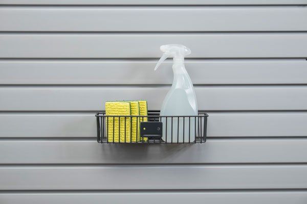 A basket filled with sponges and a spray bottle is hanging on a wall.