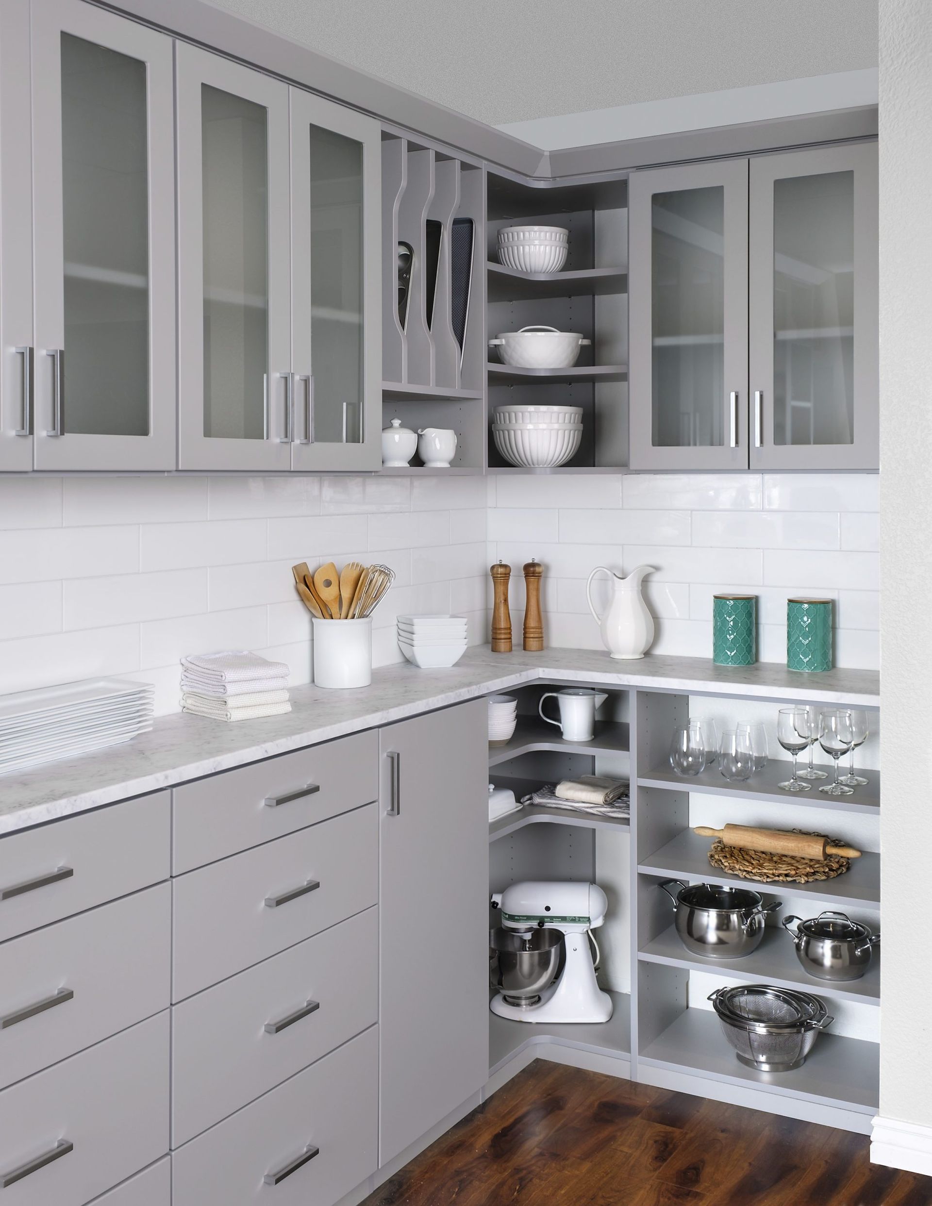 A kitchen corner featuring gray cabinetry, glass-front upper cupboards, open shelving, and a white subway tile backsplash.