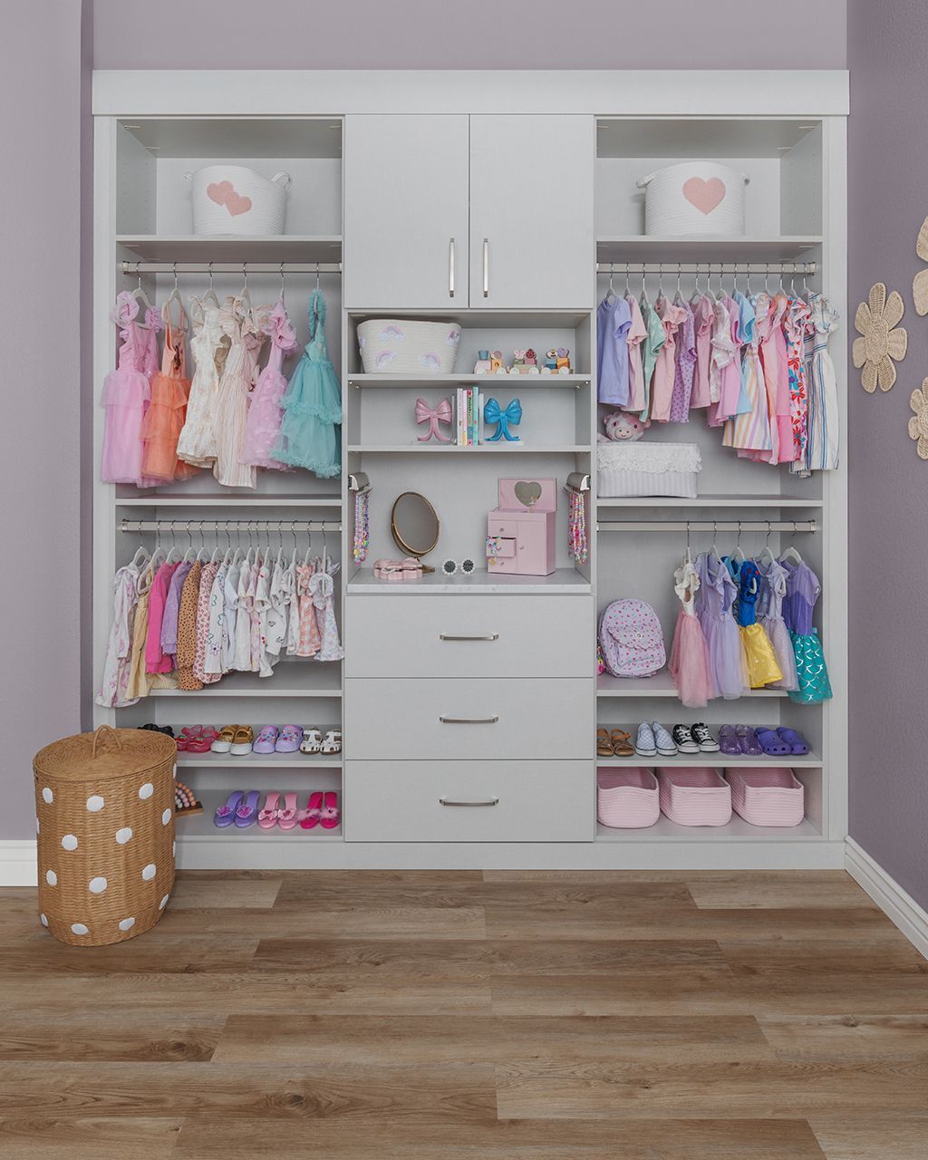 Built-in closet with pastel children’s clothes, drawers, and storage bins in a room with wood flooring
