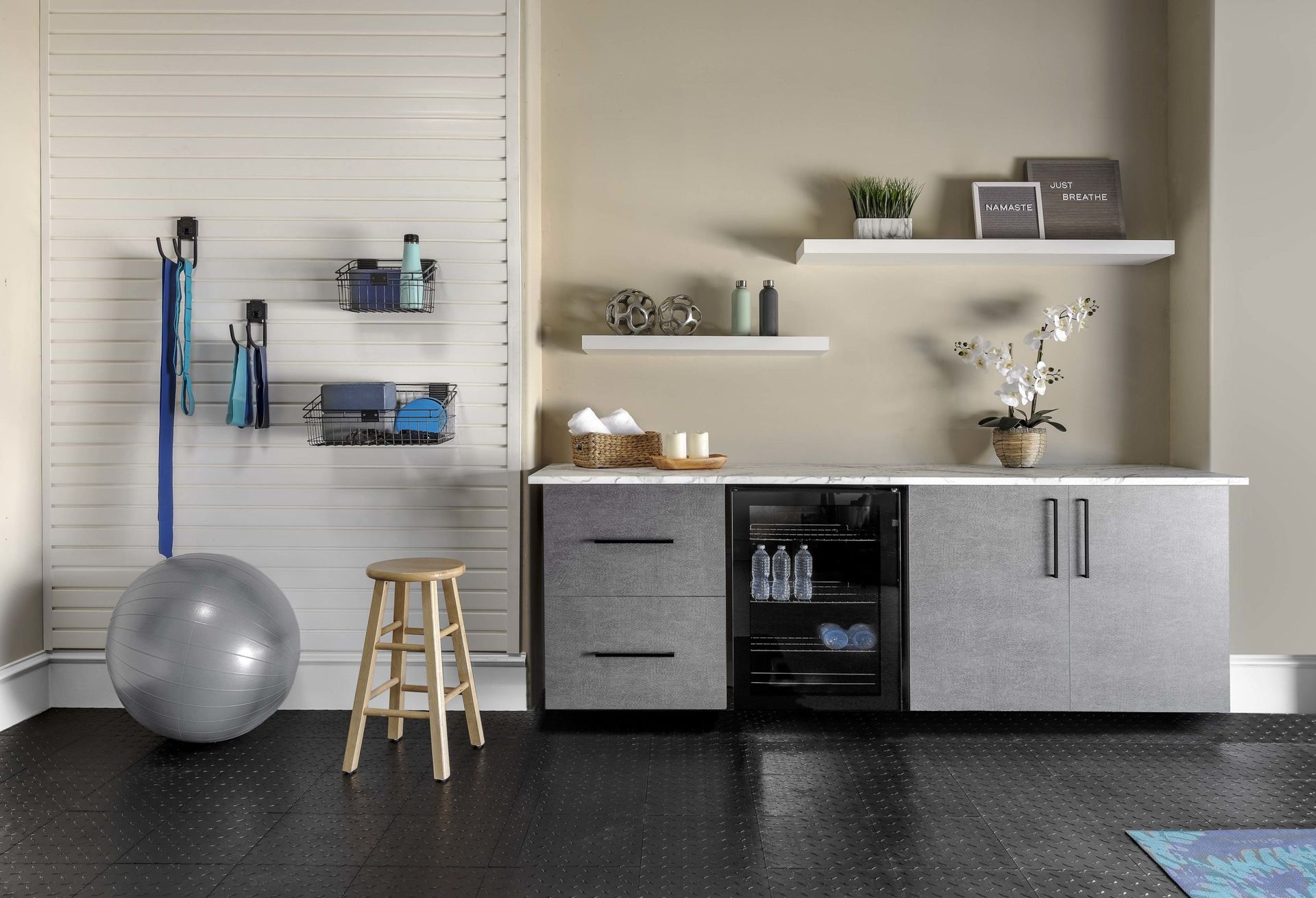 A home gym space featuring a slat wall with storage, a yoga ball, a wooden stool, and a cabinet unit with a mini-fridge.