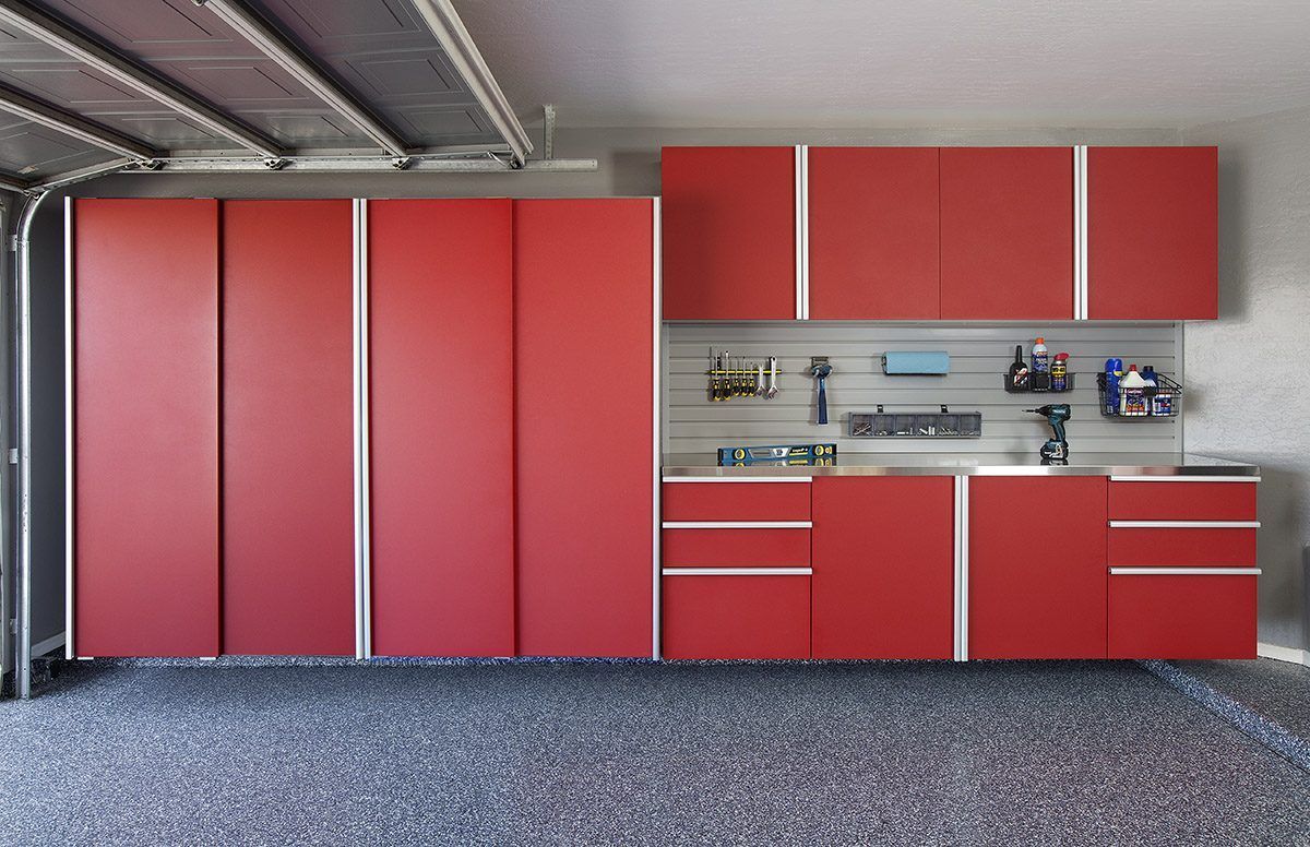 Red garage cabinets and storage system with drawers, wall-mounted racks, and a workbench on a textured gray floor.