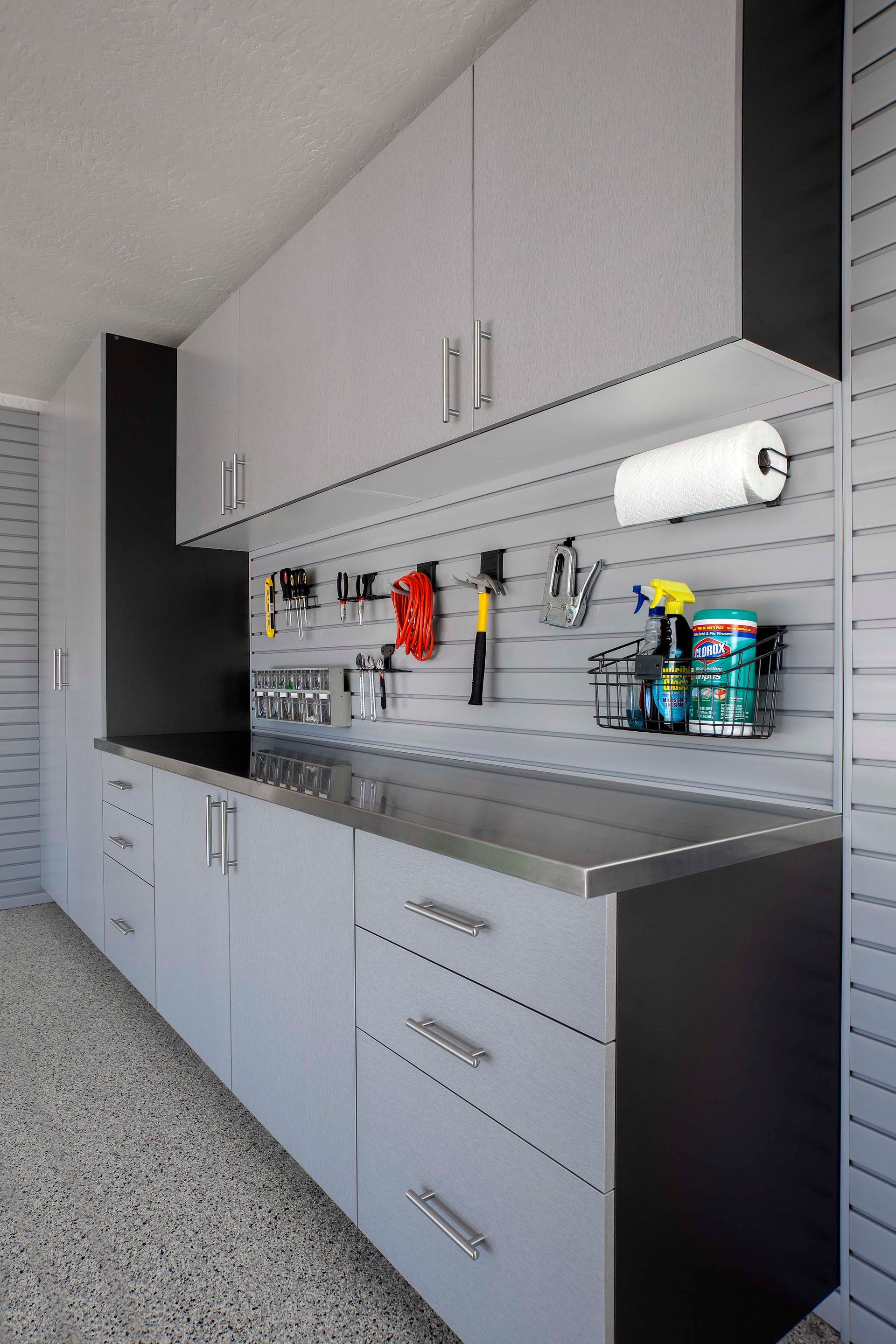 Modern gray garage cabinetry with stainless steel countertops and a slat-wall system for tool and supply organization.