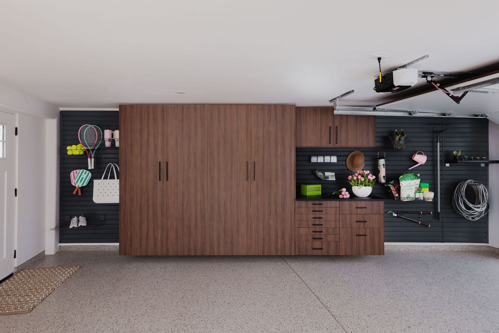A modern garage featuring wall-mounted wooden cabinets and drawers with black slat-wall storage panels and epoxy floors.