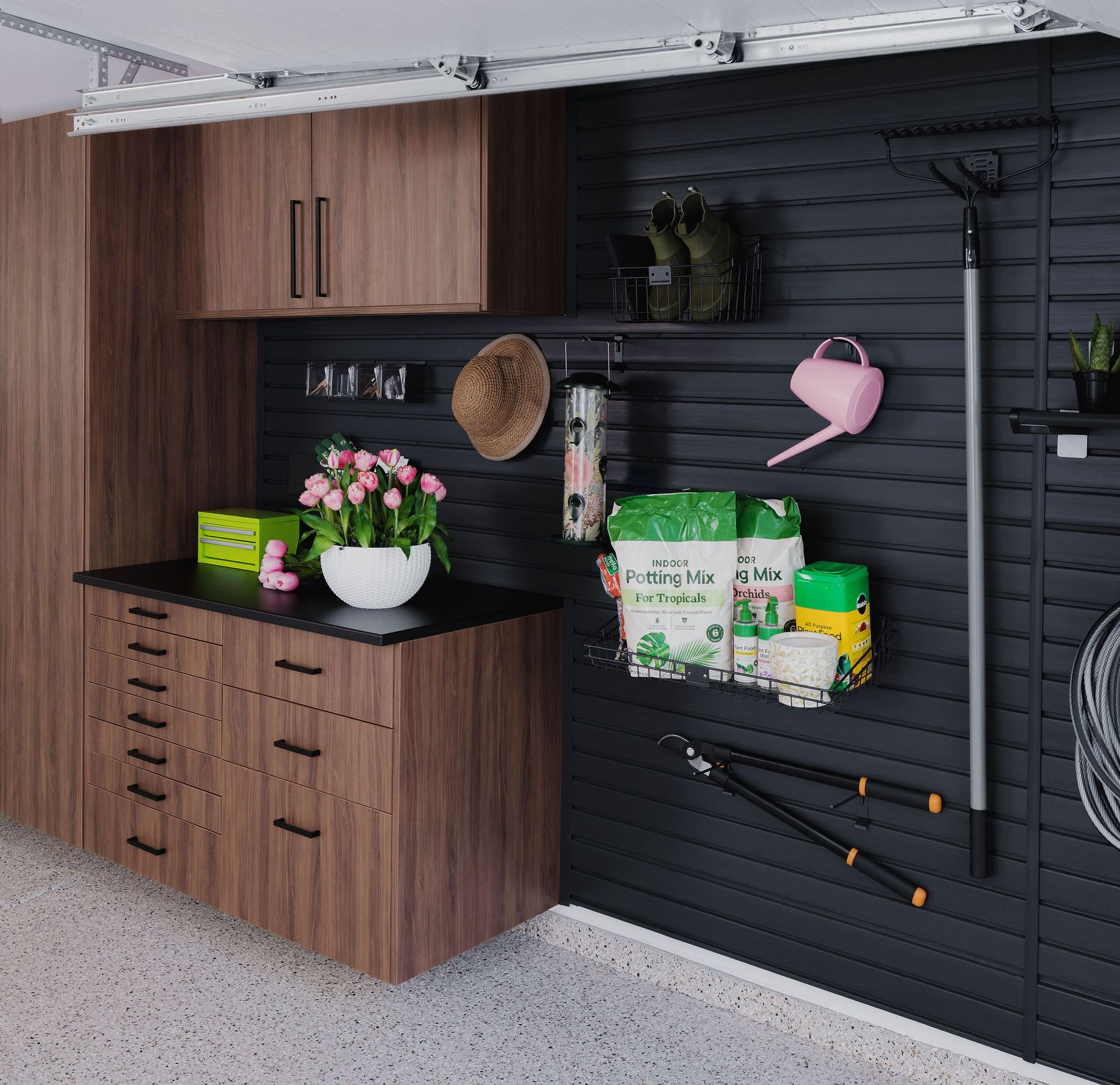 A well-organized garage workspace with dark wood cabinets, a black slat wall, and garden tools hanging on display.