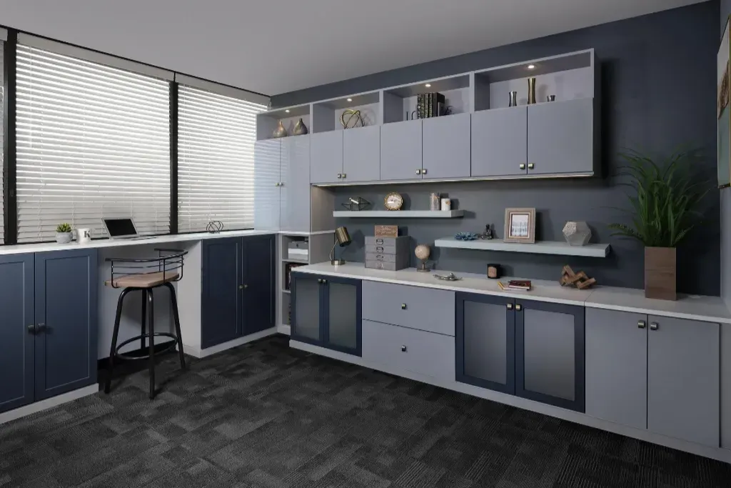 A modern home office with navy and light gray cabinets, a window-facing workspace, and open shelving on a dark wall.