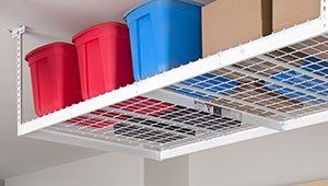 White overhead garage storage rack holding blue and red plastic bins and cardboard boxes.