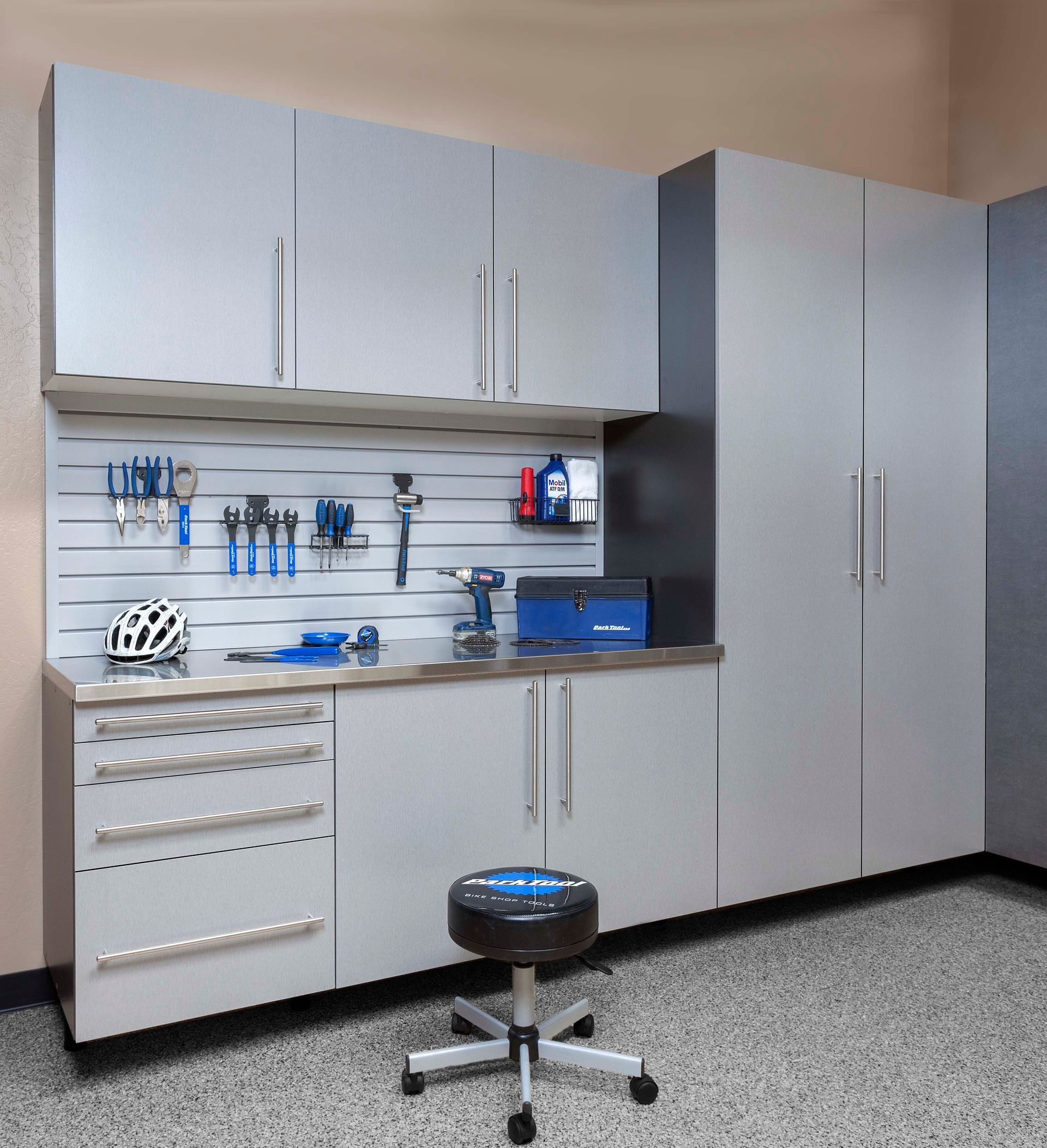 Modern grey garage storage system featuring wall cabinets, a stainless steel countertop, drawers, and a tool rack.