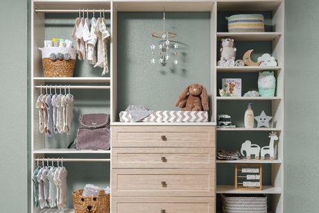A nursery closet organization system with hanging clothes, a central changing table dresser, and open shelving with toys.