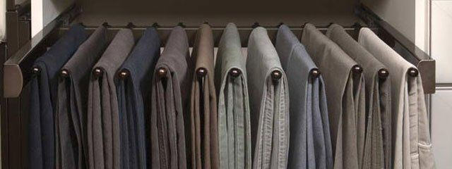 A row of pants hanging on a rack in a closet.